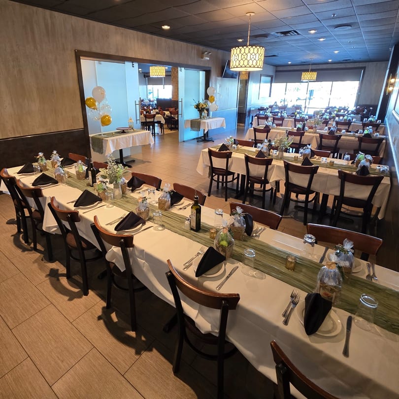 A restaurant dining room with long tables set with white tablecloths, green runners, and black napkins.