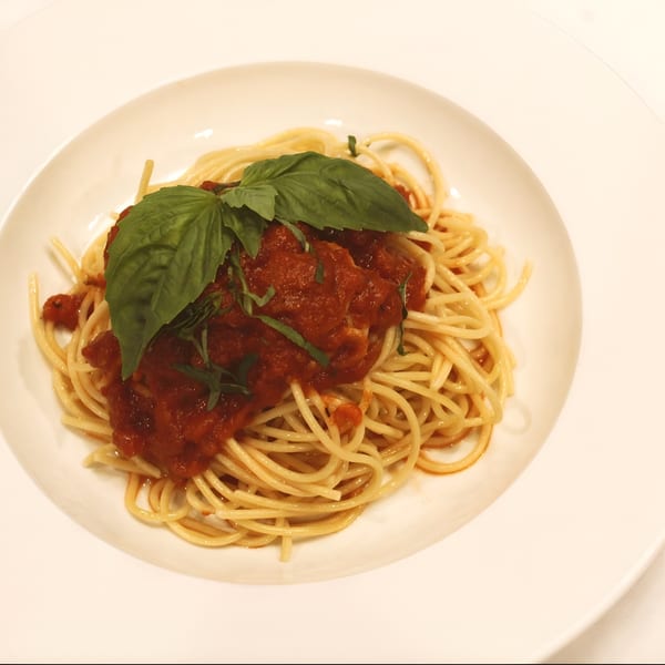 Spaghetti with red sauce and fresh basil leaves on a white plate.