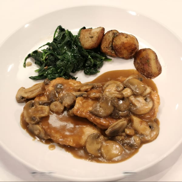 Chicken with mushroom gravy, roasted potatoes, and sautéed spinach on a white plate.