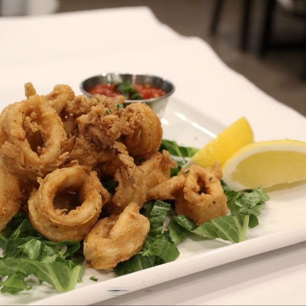 Crispy fried calamari rings and tentacles on a bed of greens with marinara sauce and lemon wedges.