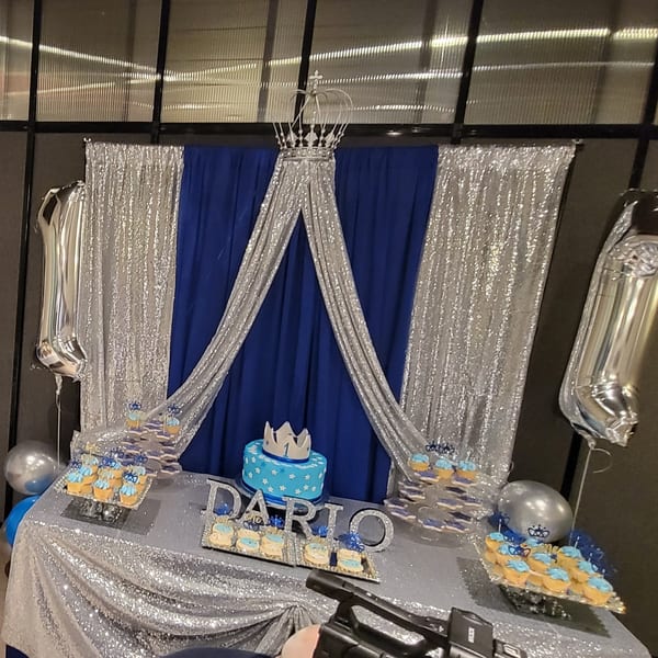 A blue and silver dessert table with a cake, cupcakes, and cookies, decorated with crowns.
