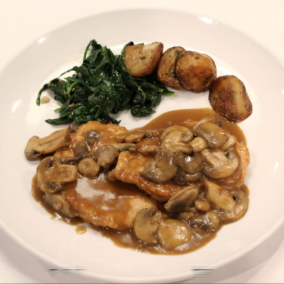 Chicken with mushroom gravy, roasted potatoes, and sautéed spinach on a white plate.