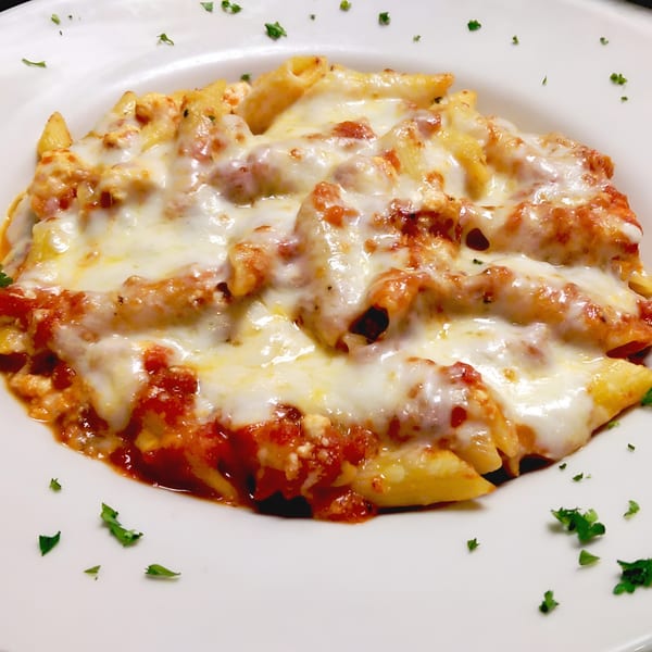 Baked ziti pasta with melted mozzarella cheese and marinara sauce, garnished with parsley.