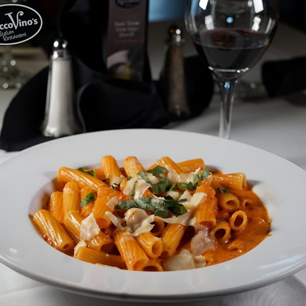 Rigatoni pasta in a creamy tomato sauce, topped with shaved Parmesan and fresh basil, with wine.