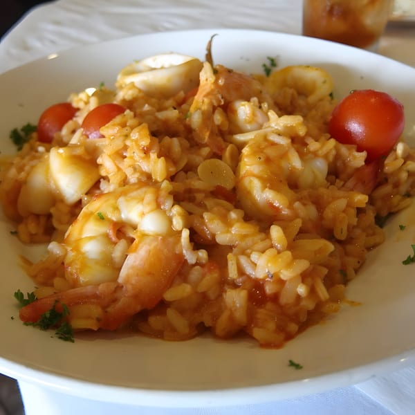 Seafood risotto with shrimp, calamari, cherry tomatoes, and parsley in a white bowl.