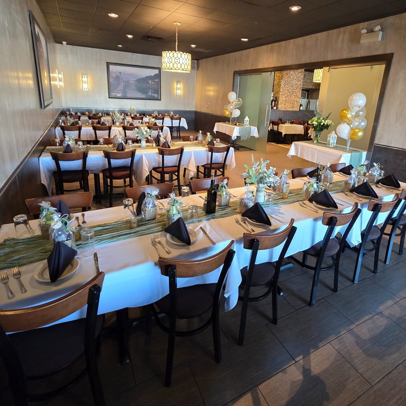 A restaurant dining room set up for an event with long tables, white tablecloths, and black napkins.