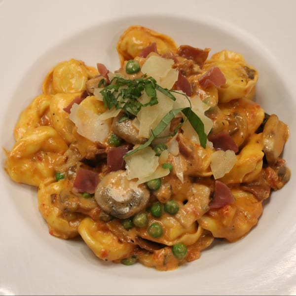 Tortellini pasta with creamy orange sauce, peas, mushrooms, prosciutto, and shaved Parmesan cheese.