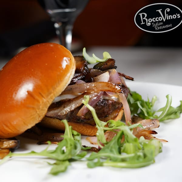 Gourmet burger with caramelized onions, mushrooms, and arugula on a white plate at RoccoVino's Italian Restaurant.
