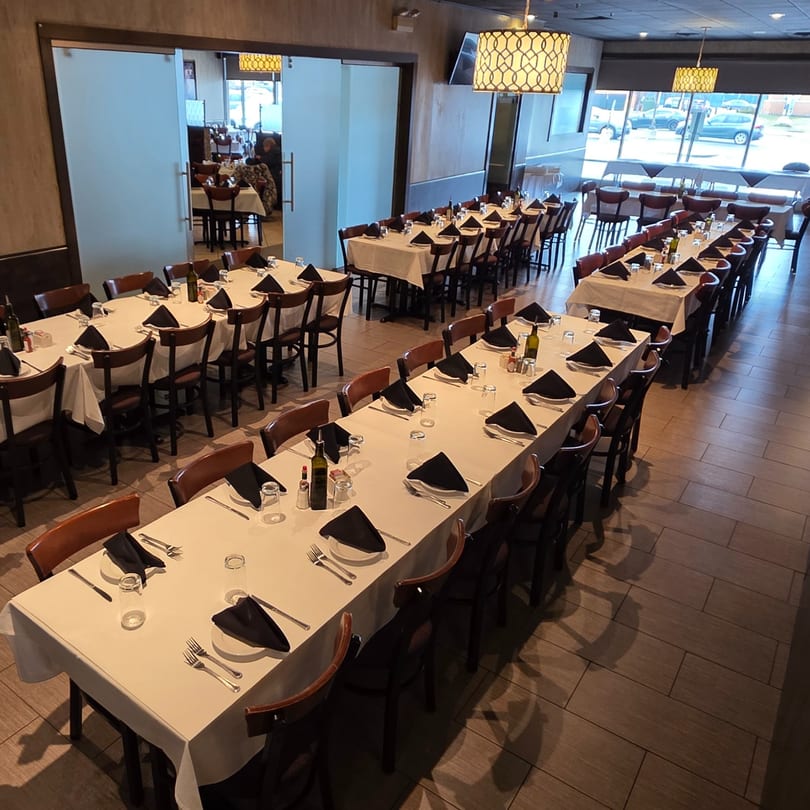 Long dining tables with white tablecloths and black napkins set for a large gathering in a restaurant.