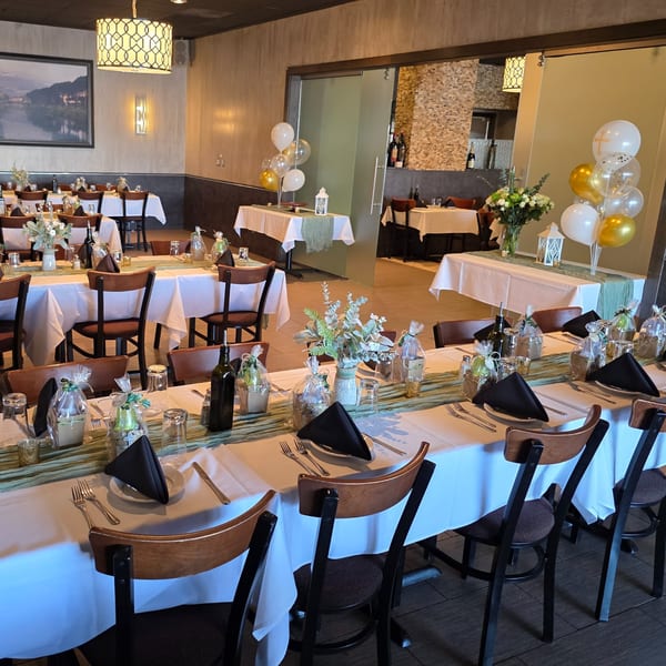 Restaurant dining room set for a party with white tablecloths, green runners, and balloons.