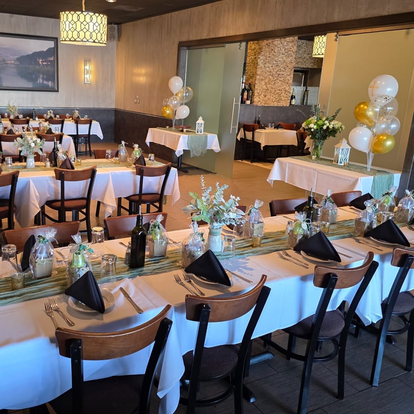 Restaurant dining room set for a party with white tablecloths, green runners, and balloons.