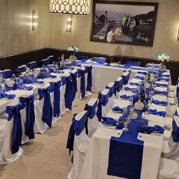 Restaurant dining room set for an event with tables draped in white and royal blue linens.